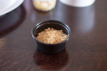 A view of a black condiment cup, featuring brown sugar.