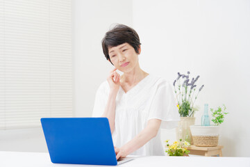 家でパソコンを見て考える中年女性