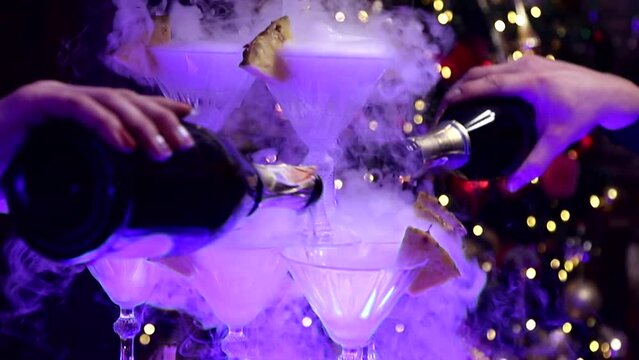 champagne is poured into a pyramid of glasses with pineapple pieces, bubbles and smoke at a christmas party