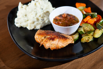 A view of a salmon dinner entree, featuring sautéed vegetables and mashed potatoes.