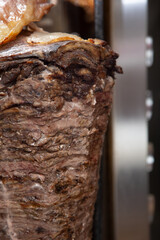 A view of a rotisserie spit machine heating up beef shawarma.