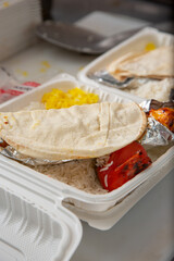 A view of the preparation of kebab entrees in plastic to-go containers, seen at in a restaurant kitchen setting.
