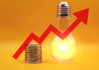 Rising energy cost concept. Light bulb on top of a stack of gold coins and red arrow.