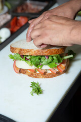 A view of a cook preparing a tuna salad sandwich at the ingredient station of a restaurant kitchen.