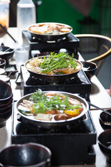 A view of a table featuring several hot pots on portable stoves, seen at a local restaurant.