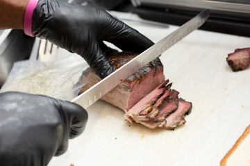 A view of a worker carving a brisket slices, in a restaurant setting.
