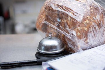 A view of a deli counter lifestyle scene, featuring a service, bell, packaged bread loaf, pen, and order notebook.
