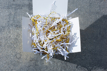 A top down view of a gift box with gold and white crinkle cut paper stuffing.