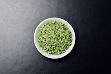 Fresh fennel seeds in bowl on dark background