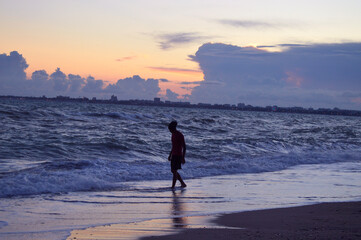The silhouette on a beach. There is a man walks on the beach of Black sea. There is a town in the background. Sunset.