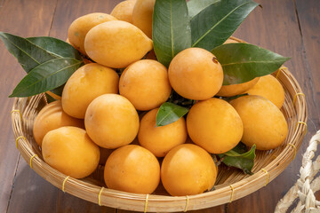 Sweet Yellow Marian Plum Or Mayong chid with leaf tropical fruite in baboo basket on wooden table.