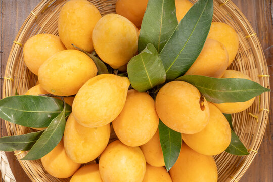 Sweet Yellow Marian Plum Or Mayong chid with leaf tropical fruite in baboo basket on wooden table.