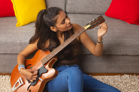 Young woman tuning guitar while sitting in living room