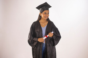 Portrait of young woman in graduation gown holding certificate while standing against white background
