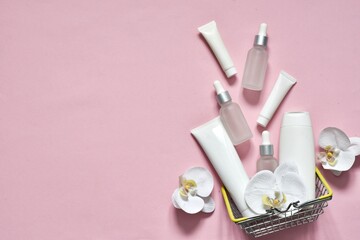 Obraz na płótnie Canvas White tubes and bottles with pipettes for cosmetics products in shopping basket on a pink background with orchid flowers. Shopping. Mockup. Copy space. Advertising natural cosmetic.