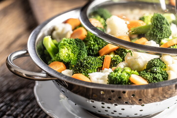 Steamed broccoli, carrots and cauliflower in a stainless steel steamer with a lid