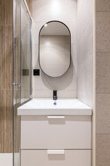 Closeup of a bathroom alcove with bright artificial lighting, with a white solid ceramic sink on a...