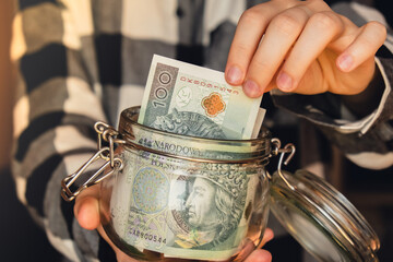 Polish zloty banknote saving money in glass jar. Unrecognizable woman moderate consumption and...