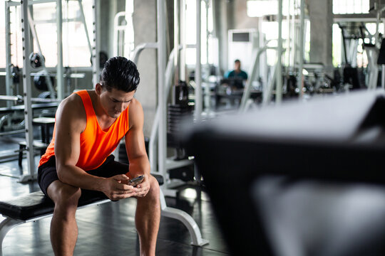 Caucasian athletic man relax sitting and texting message on smartphone at gym fitness. serious male using mobile phone in sport club before workout exercise  