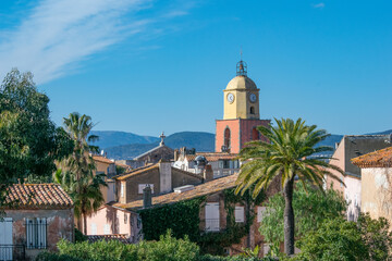 Saint Tropez church tower with rooftops and palm trees against blue sky