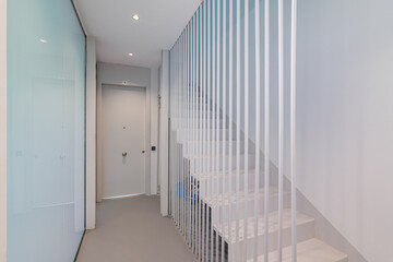 White staircase to the second floor with soft blue lighting in a modern building. Original design solution of the floor-to-ceiling fence made of metal white rods gives the effect of weightlessness.
