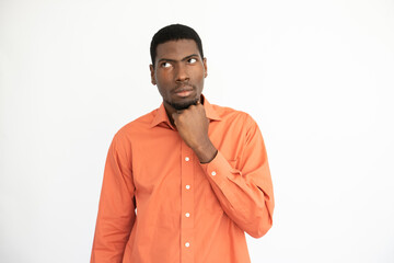 Portrait of thoughtful young man looking away over white background. African American guy wearing orange T-shirt posing with pensive expression. Thinking and planning concept