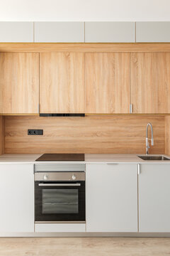 Closeup Of Piece Of Modular Kitchen Furniture Made Of Light Wood. Modern Cozy Kitchen Interior With Appliances Built Into Marble Countertop. Hood Hidden From View In Cabinet Above Stove.