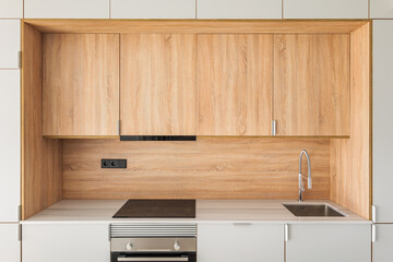 Close-up of metal sink and faucet at contemporary minimal kitchen. Wooden furniture at empty refurbished apartment