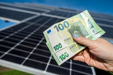 beautiful young well-groomed hands hold a large sum of euros near installed solar panels.