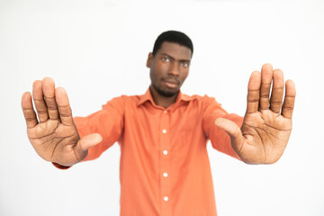 Fototapeta premium Close-up of male hands making stop gesture over white background. African American guy wearing orange T-shirt showing forbiddance sign. Restriction concept