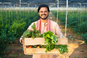 Happy smiling young farmer carrying basket of vegetables for market at green house - concept of...