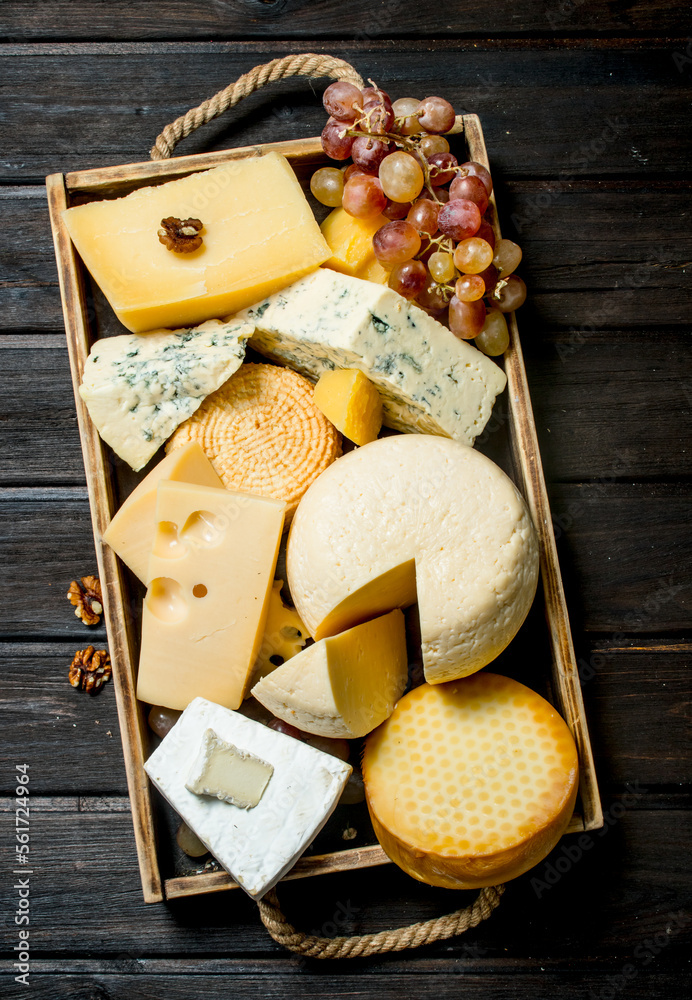 Wall mural different types of cheese in a wooden tray with grapes .