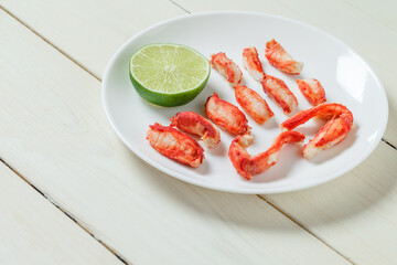 Crab meat slices phalanges and lime on plate on white wooden board background, selective focus