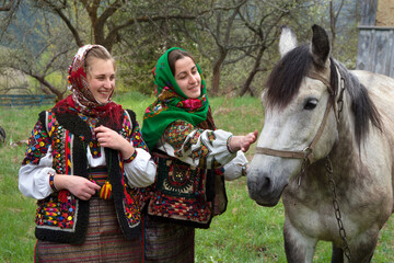 Young girls dressed in ancient picturesque hutsul national clothes caress the horse. Ukraine.