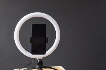 A blank screen of smartphone fixed on a round lamp or ringlight on a tripod for video recording...