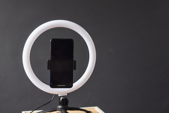 A blank screen of smartphone fixed on a round lamp or ringlight on a tripod for video recording with phone 