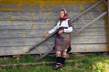 Ukrainian woman in an authentic Hutsul costume stands near a ladder on the background of a wooden...