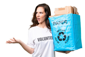 Young caucasian woman holding a recycling bag full of paper to recycle over isolated background with surprise facial expression