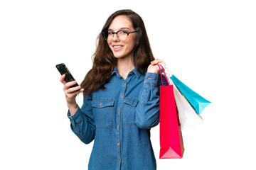 Young caucasian woman over isolated background holding shopping bags and writing a message with her...