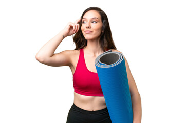 Young sport woman going to yoga classes while holding a mat over isolated background having doubts and thinking