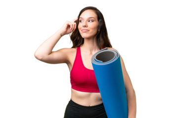 Young sport woman going to yoga classes while holding a mat over isolated background having doubts and thinking