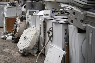 Dump or collection point for broken washing machines and spare parts on ground in open air. Assembling obsolete household appliances that are out of order for utilization and recycling of plastic