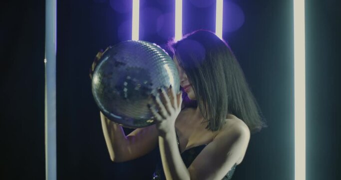 Portrait of gorgeous woman dancing with disco ball in night club with neon illumination. Youth lifestyle and enjoyable nightlife concept.