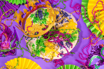 King Cake for Mardi Gras, traditional New Orlean Mardi Gras holiday pastry with plastic baby, with festival masquerade accessories, decor, carnival mask, beads © ricka_kinamoto