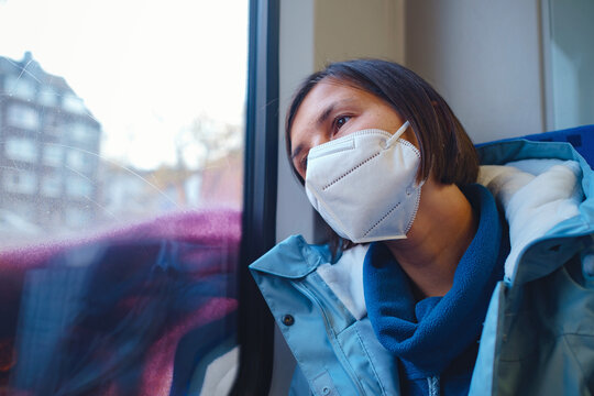 Asian Woman in blue jacket and protective mask looking out of train window in winter day. Lifestyle concept.