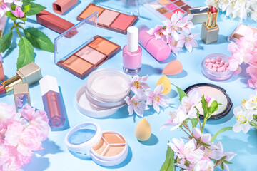 Spring make up set on light blue background. Different make-up professional cosmetics, beauty accessories flat lay with spring blossom flowers top view copy space