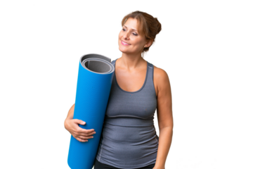 Middle-aged sport woman going to yoga classes while holding a mat over isolated background looking to the side and smiling