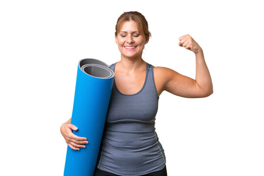 Middle-aged sport woman going to yoga classes while holding a mat over isolated background doing strong gesture