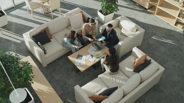 High angle view of group of business people sitting on sofas around table and discussing project in team in office hall