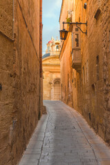 Old medieval narrow empty street with street lights in Mdina town, Malta. Vertical orientation. Travel destination